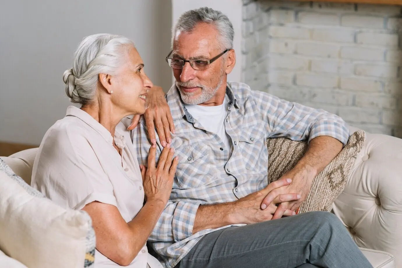 Smiling elderly couple seated on a sofa, looking at one another.