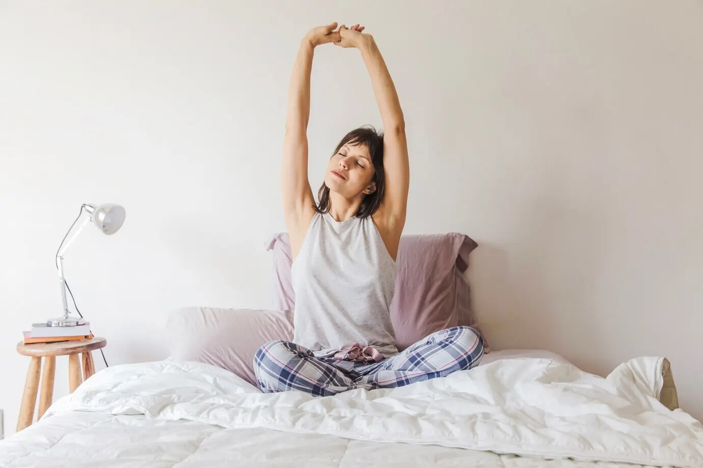 In the morning, a woman stretches her arms on the bed.