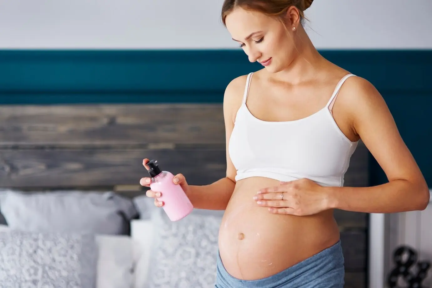 A young pregnant woman applying cream to her belly.