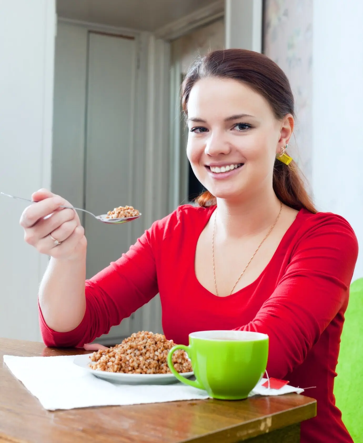 A happy girl wearing red eats buckwheat.